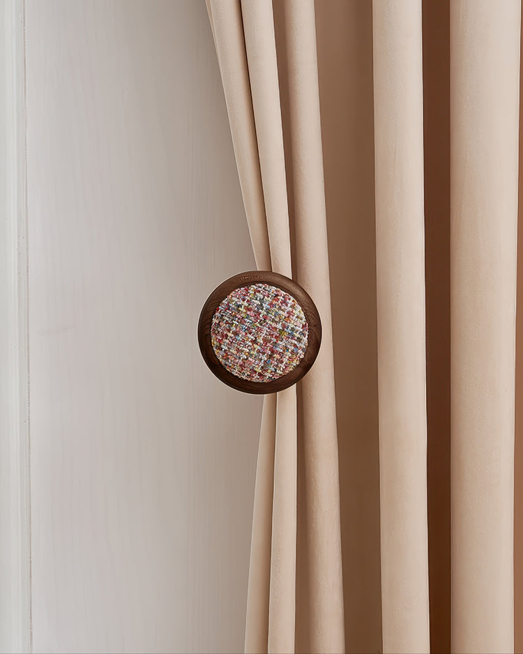 Round wooden curtain wall hook with colorful sweater yarn inlay holding back a beige velvet drapery panel.