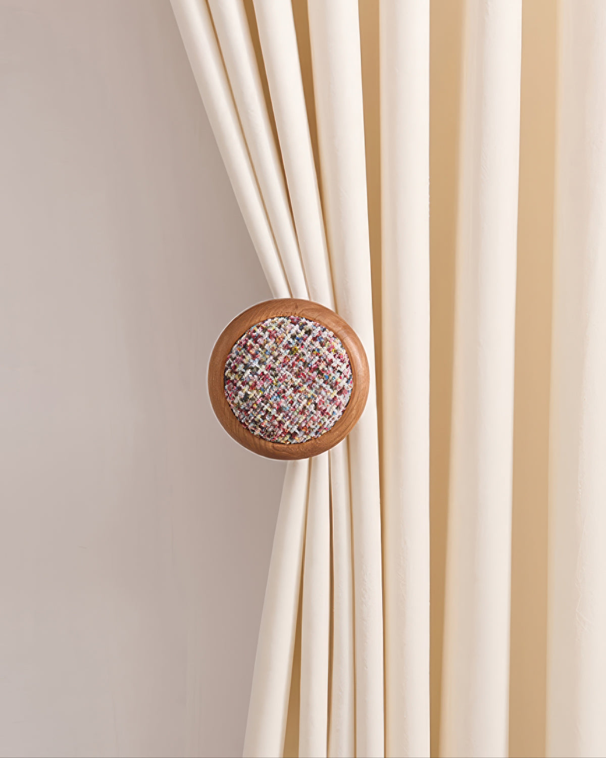 Elegant cream drapery secured by a sophisticated wooden curtain wall hook with colorful tweed yarn insert.