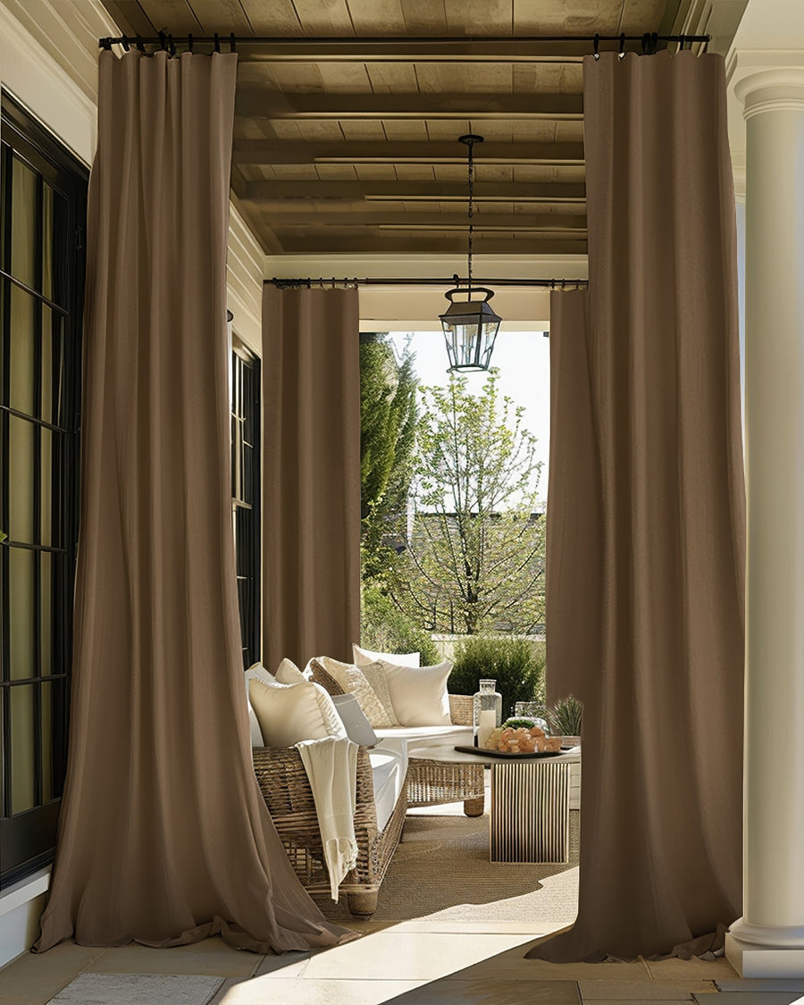 Two brown FadeShield Pro outdoor blackout curtains on a cozy patio, providing privacy and weather protection for a wicker seating area.