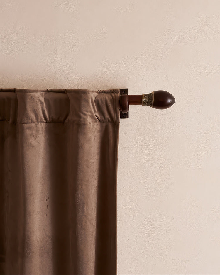 Close-up of a dark wood custom curtain rod with an ornate carved finial, featuring a decorative brass band, paired with brown velvet drapery.