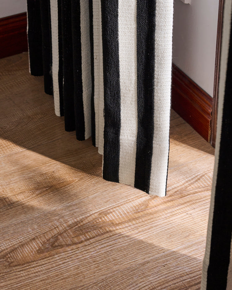 Liam Striped linen blend custom curtain with bold black and white woven stripes, resting on a rustic wood floor.