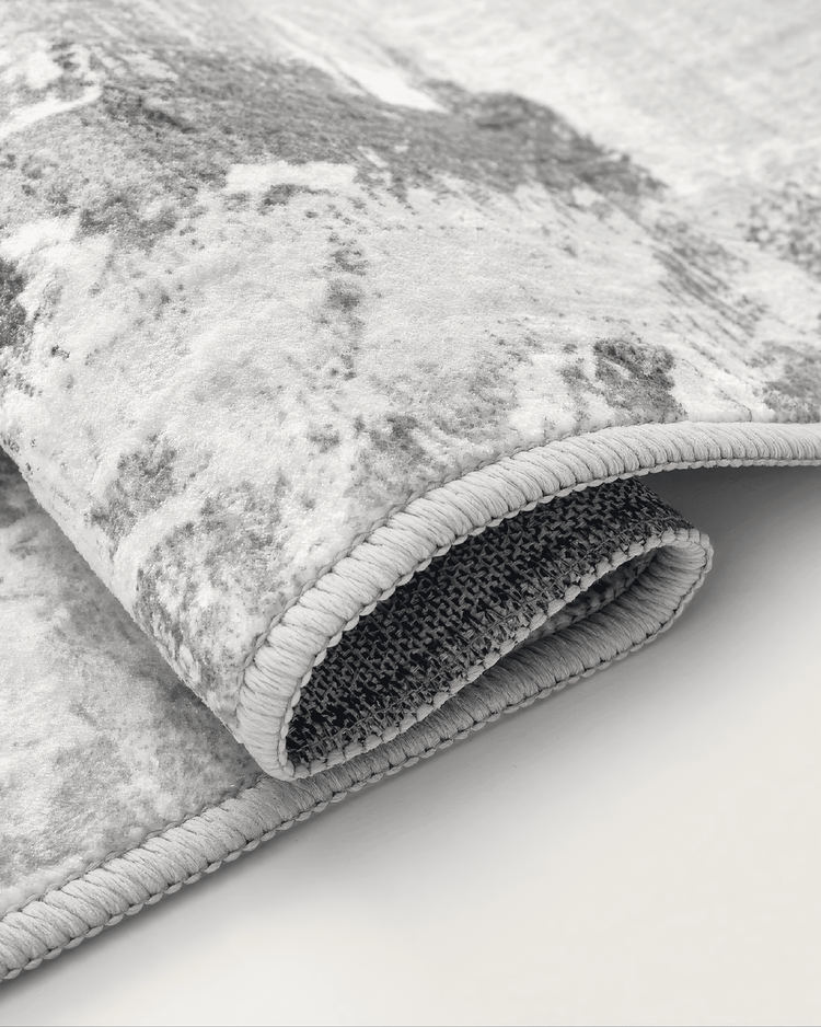 Rolled Tara Dark Gray washable area rug showing its vintage geometric pattern, soft texture, and light grey edge binding with durable backing.