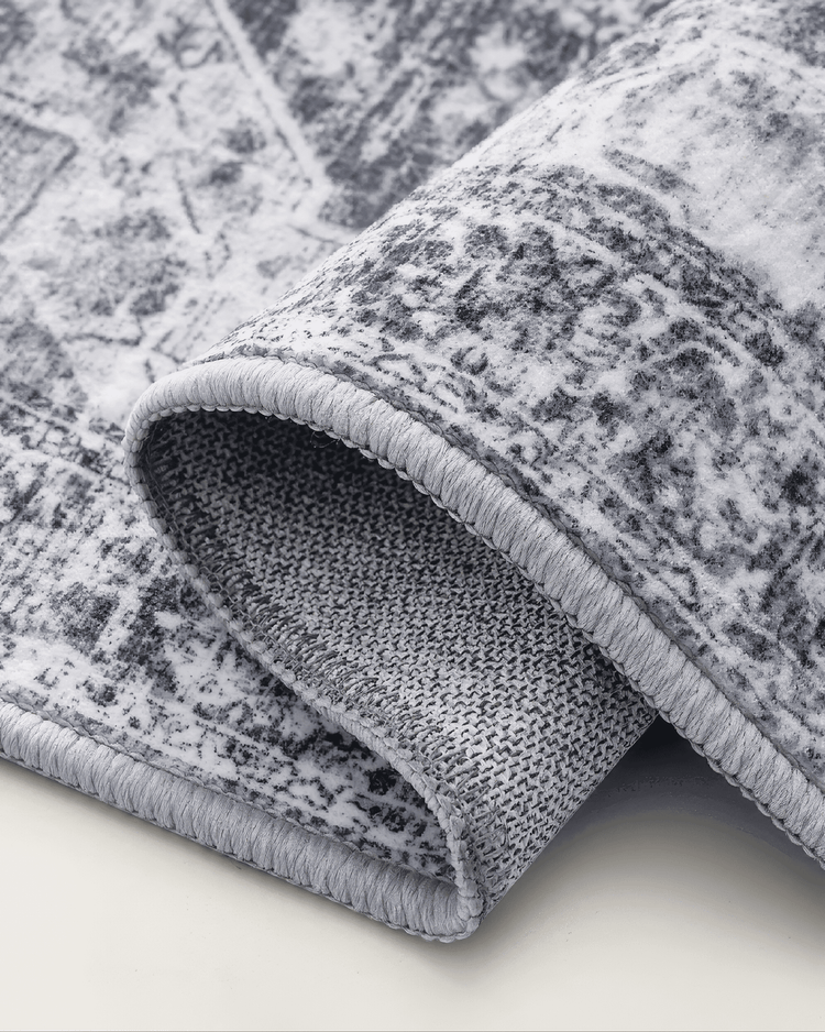 Rolled Diana's Garden Denim Blue washable area rug, showcasing its distressed pattern, light grey bound edge, and non-slip backing.