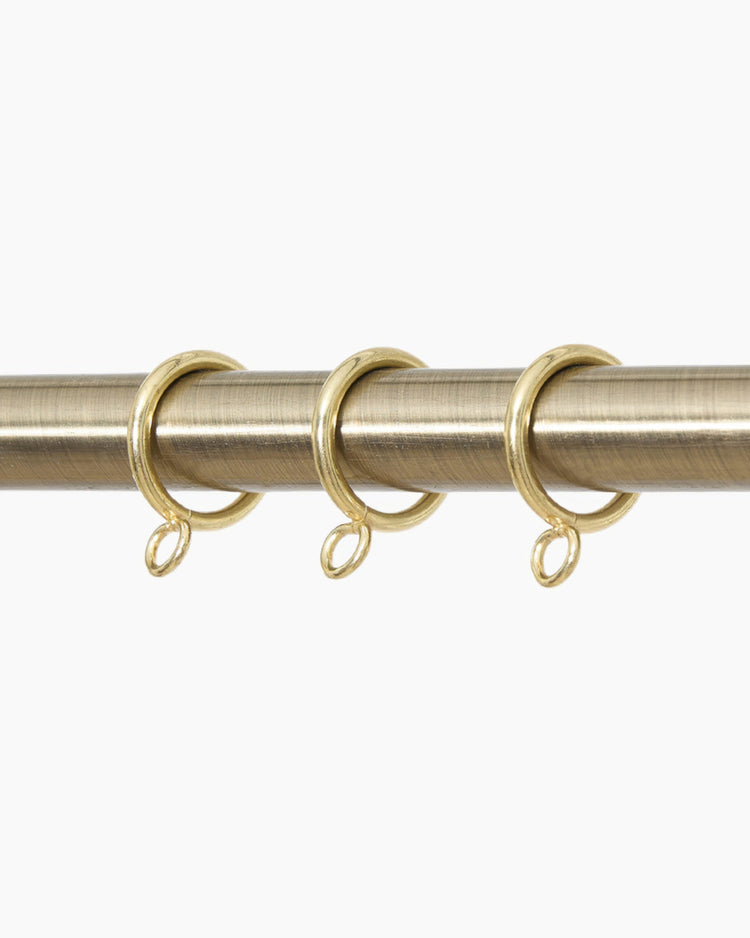 Three antique brass hanging rings with eyelets on a matching curtain rod for custom drapery & window treatments.