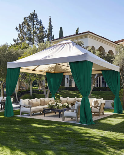 Lush garden patio featuring a white gazebo with tied-back FadeShield™ green waterproof custom outdoor curtains, providing privacy for luxury lounge seating.