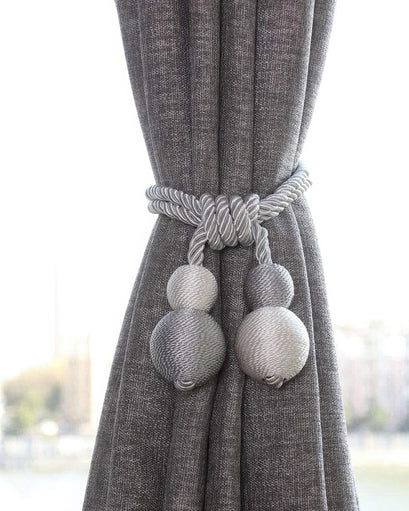 Luxurious silver rope ball curtain tieback elegantly cinching a textured charcoal grey drapery panel, for high-end custom window treatments.