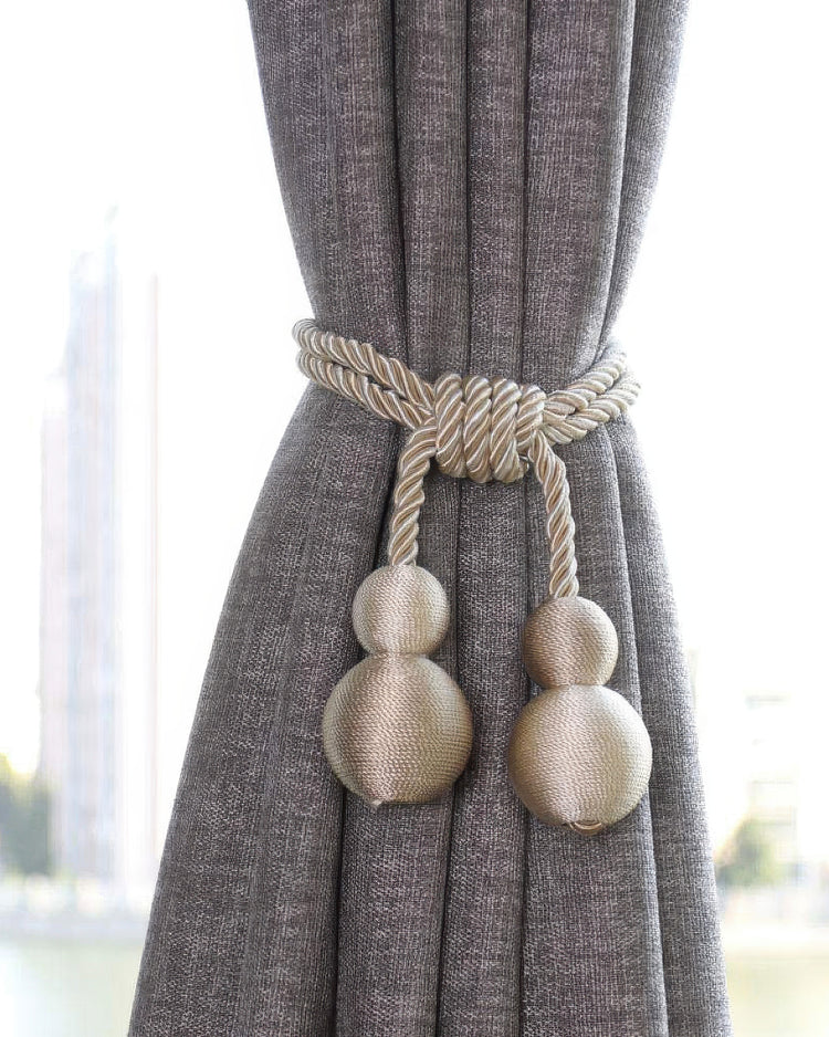 Elegant gold braided rope curtain tieback with spherical tassels securing a custom grey textured blackout drapery.