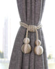 Elegant gold braided rope curtain tieback with spherical tassels securing a custom grey textured blackout drapery.