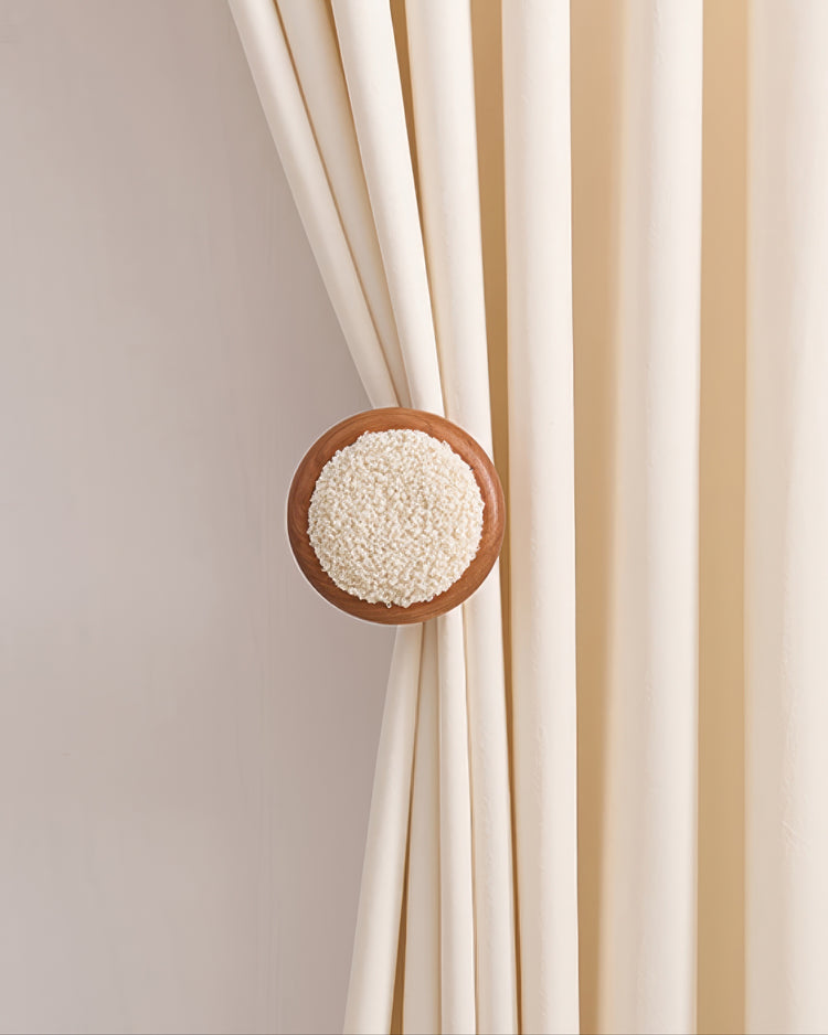 Cream velvet drapery pulled back by a circular leather knob curtain wall hook with a white boucle textured center.
