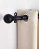 Classic black adjustable curtain rod with elegant round ball finial, securely holding a textured beige grommet drapery.