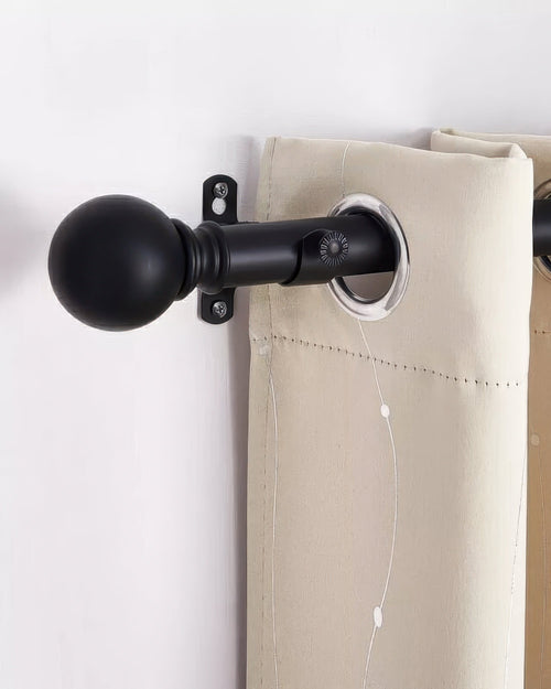 Black classic ball adjustable curtain rod with round finials, mounted on a wall, holding elegant beige grommet drapery.