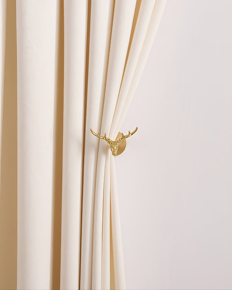 Golden deer head metal curtain wall hook decoratively holding back an elegant creamy white custom drapery.