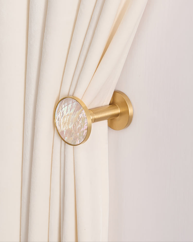 Gold brass seashell curtain wall hook holds back cream velvet drapery. Iridescent mother-of-pearl inlay for custom window treatments.