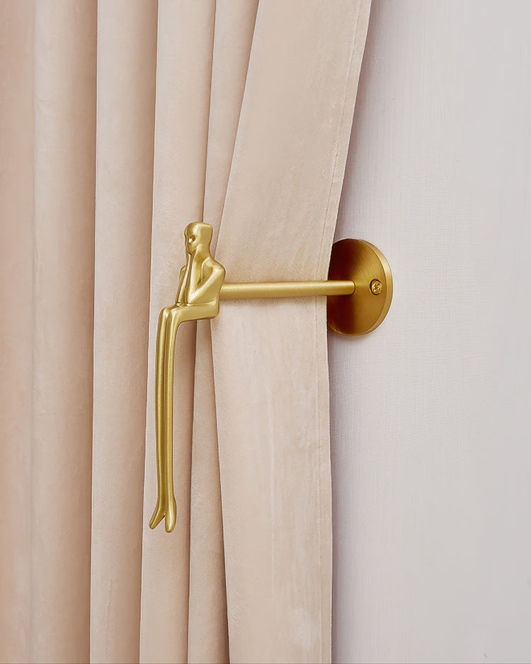Decorative gold mannequin metal curtain wall hook holding back a plush beige velvet drapery panel.