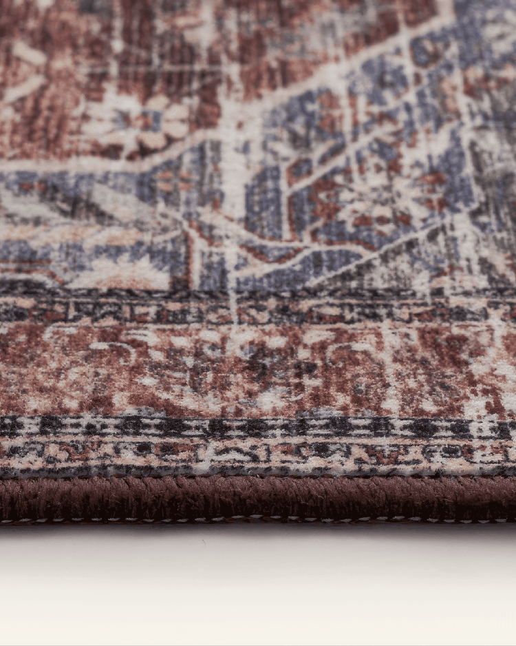 Close-up of Diana's Garden washable area rug showing detailed distressed red, blue, cream Persian pattern & brown stitched border.