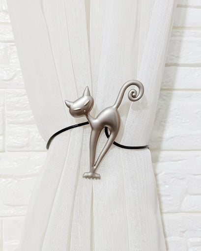 Stylized silver cat magnetic curtain tie-back securing a sheer white drapery panel. Modern window treatment accessory.