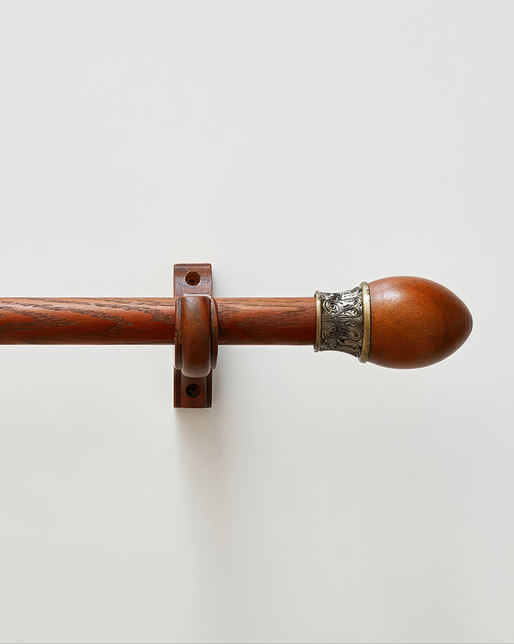 Carved custom wooden curtain rod with ornate finial and matching bracket against a white wall for elegant home decor.