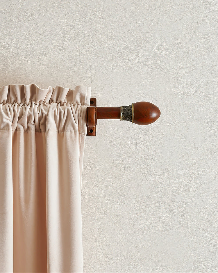 Elegant carved custom wooden curtain rod with an ornate brass and wood finial, supporting light beige velvet gathered header drapery.