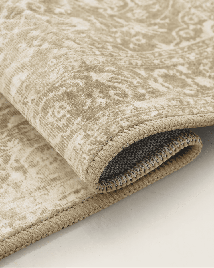 Rolled neutral antique washable area rug, highlighting its soft, distressed pattern, bound edge, and flexible backing.