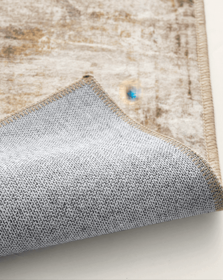 Close-up of Mystic Clouds warm beige washable area rug, showing its textured non-slip backing and detailed edge stitching.