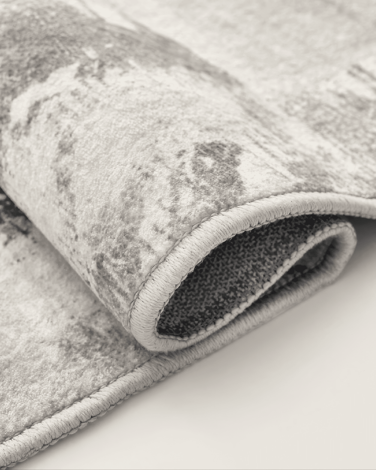 Rolled Geometric Vintage Tara Washable Area Rug close-up, highlighting its soft texture, distressed pattern, and durable stitched edge.