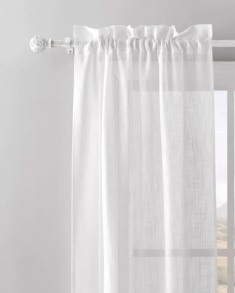 White sheer window treatment with textured pattern hanging on an antique adjustable white curtain rod with decorative finial.