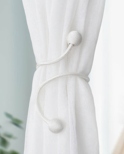 Modern silver curtain tie-back with unique textured spherical ends and a coiled rope design, cinching elegant white sheer drapery.