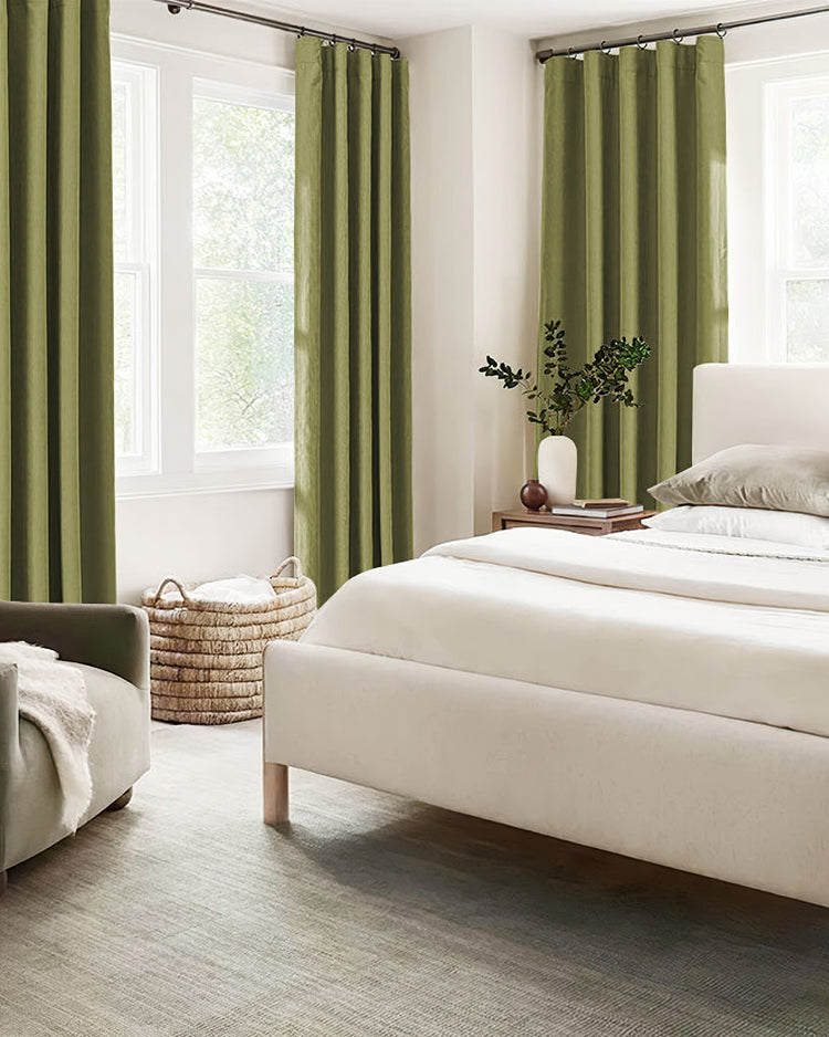 Green herringbone chenille blackout custom curtains frame two large windows in a bright bedroom, ensuring thermal comfort and soundproofing.