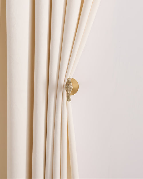 High-end cream velvet drapery gracefully held by a golden bird metal curtain wall hook, enhancing sophisticated home decor.