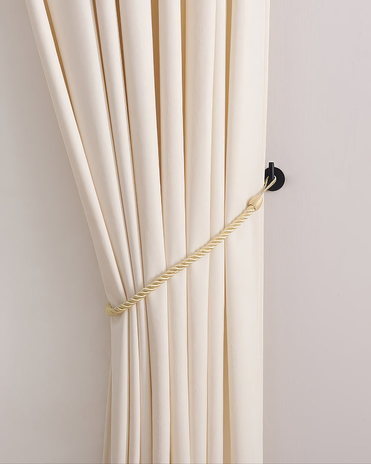 Cream drapery held by a decorative gold rope tie-back on a modern black curtain wall hook, enhancing window treatments.