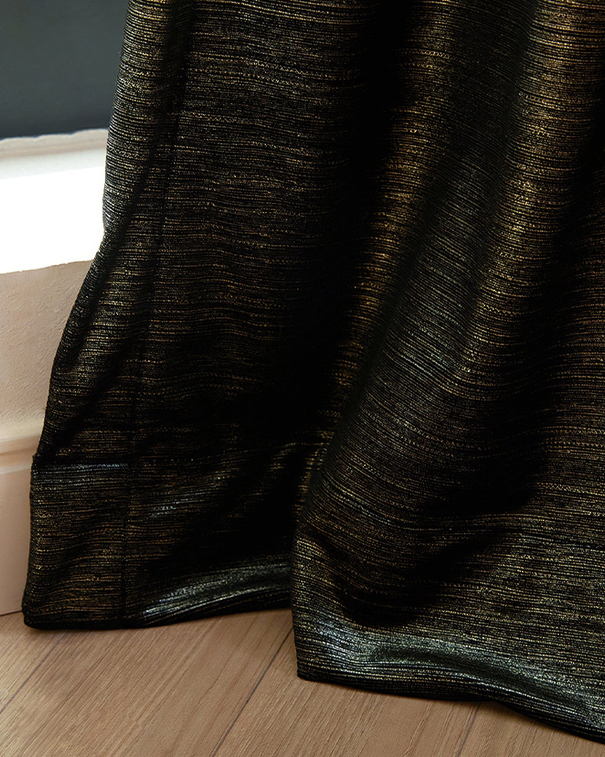 Close-up of luxurious Rome custom velvet curtain, black with horizontal gold foil print, drapes elegantly on wood floor.