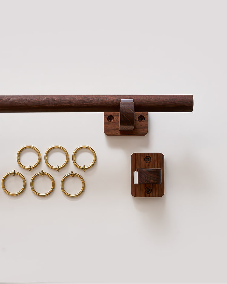 Minimalist dark wood curtain rod set with stylish wall mounts and six brass drapery rings for custom window treatments.