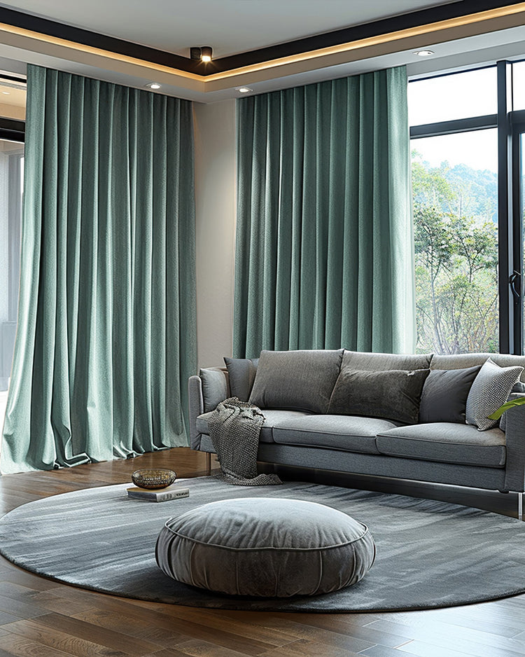 Lush sage velvet custom blackout curtains in a living room, framing a large window with a grey sofa & elegant round rug.