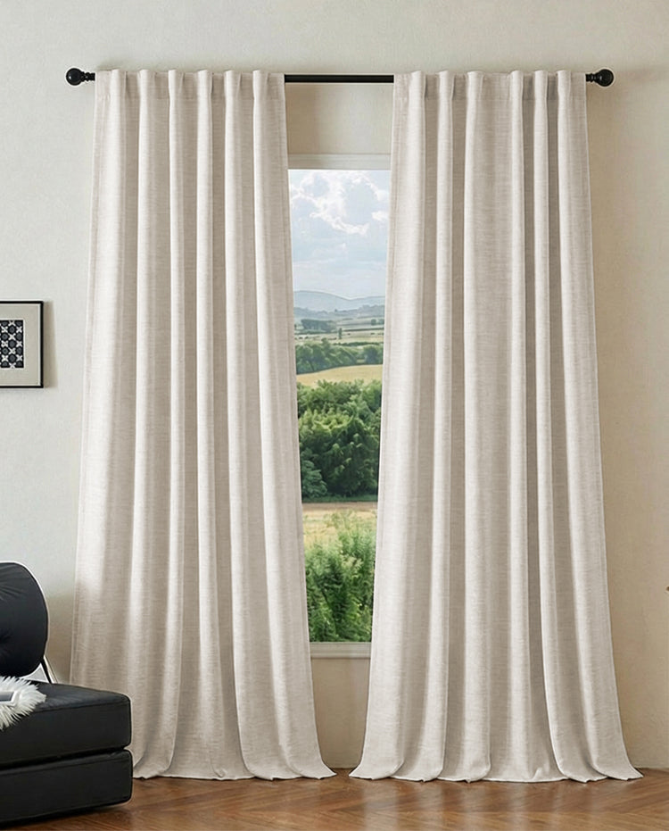 Elegant cream pleated custom blackout jacquard curtains, hung on a black rod, framing a lush outdoor view, for sophisticated home decor.