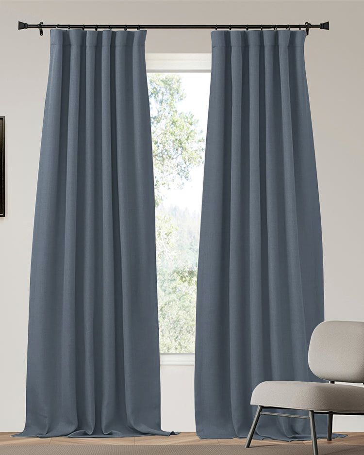 Zoe custom blackout curtains in dense slate blue linen-look fabric, heavyweight with precise pleats, beautifully framing a sunlit window.