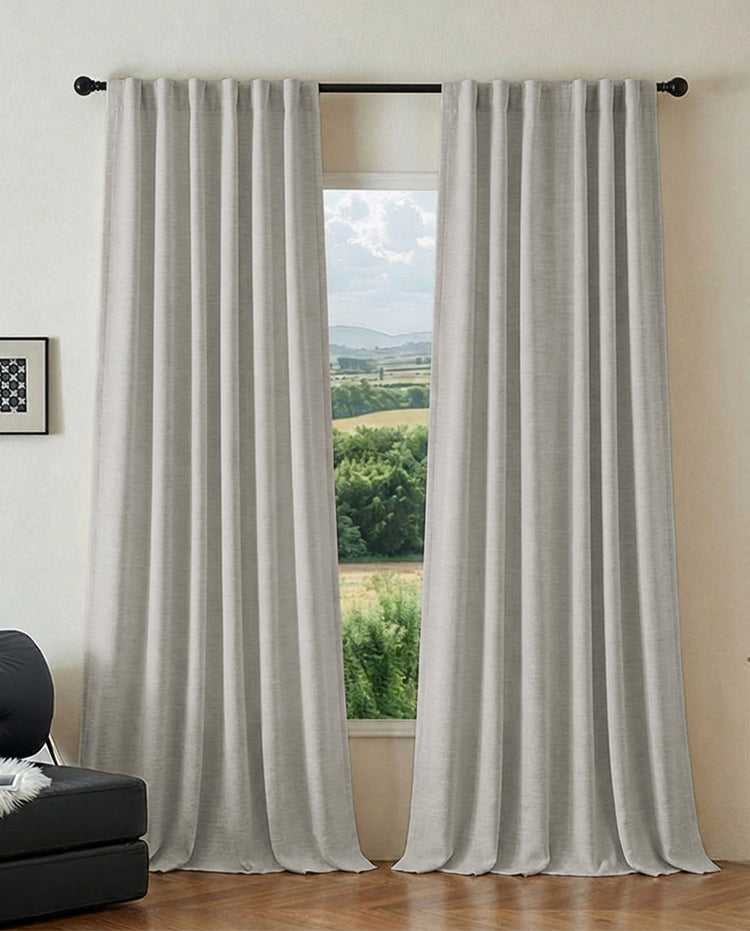 Greige jacquard custom pinched pleat curtains, heavyweight & thermal, on a black rod, open to a window with a green landscape view.