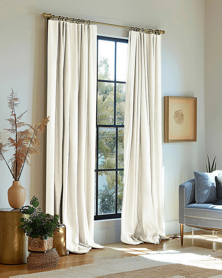 Heavyweight off-white woven textured blackout drapery on a gold rod in a sunny living room, offering tailored light control.