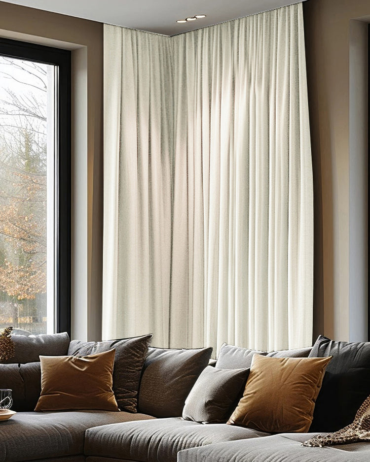 Florence light beige custom blackout curtains with a woven texture and ripple fold header on a corner window in a living room over a sofa.