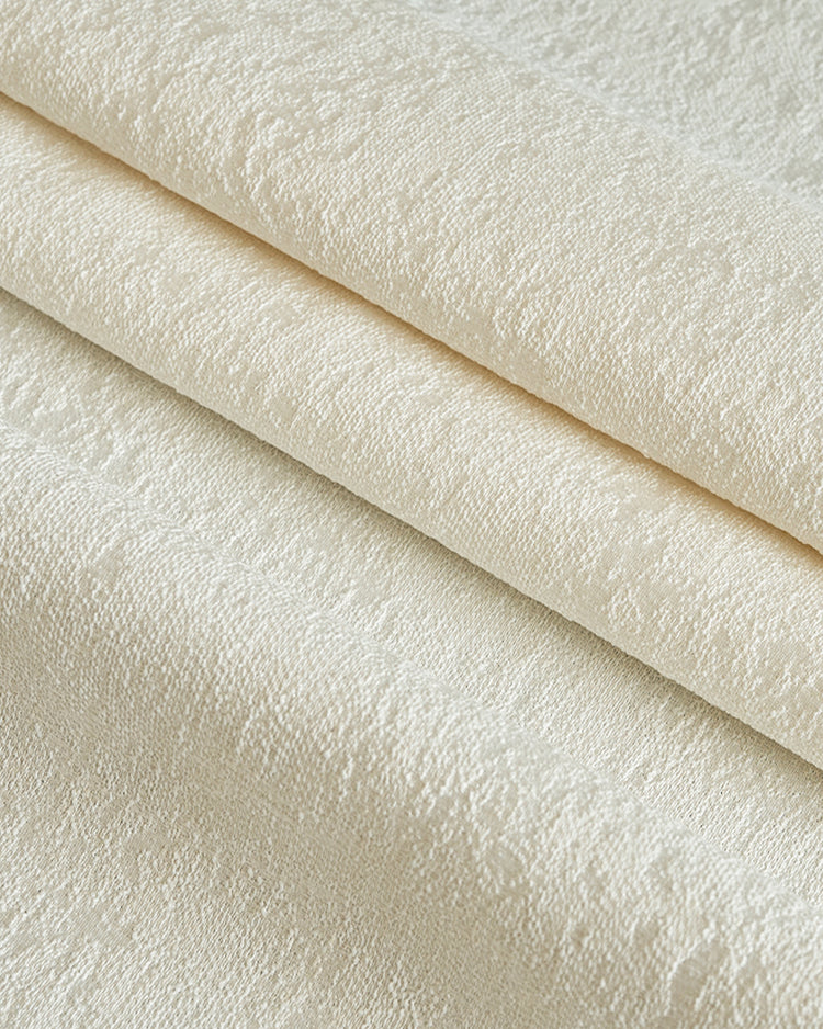 Close-up of folded cream jacquard fabric for custom blackout curtains, highlighting heavyweight texture for soundproof thermal privacy.