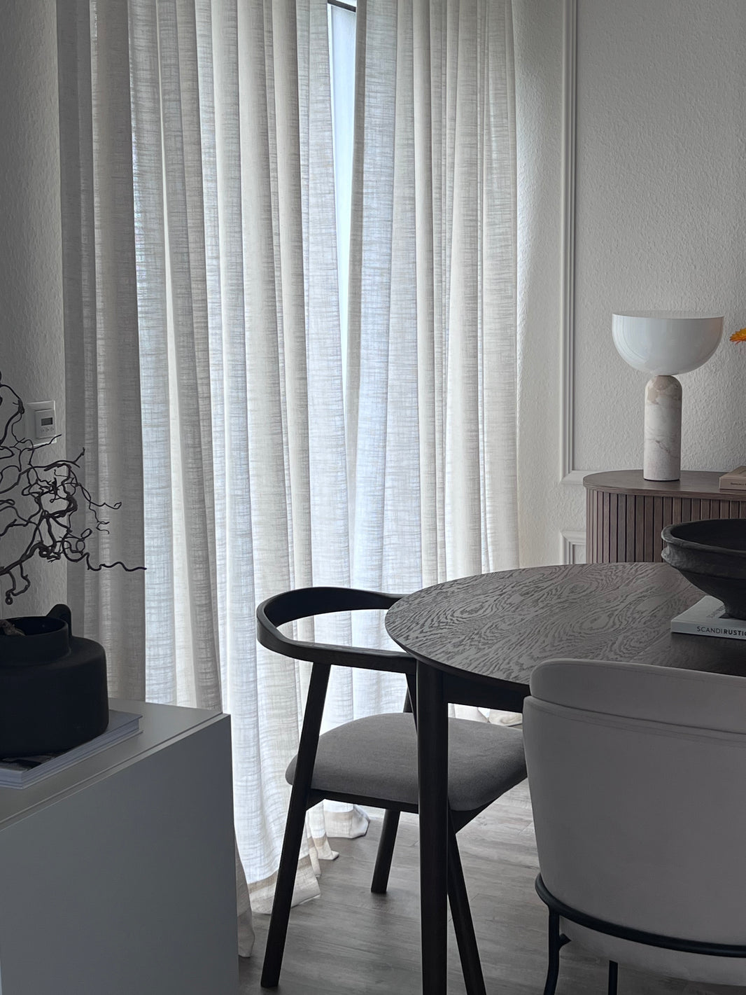 Round dining table with chairs in a room with white walls and a window with blinds.