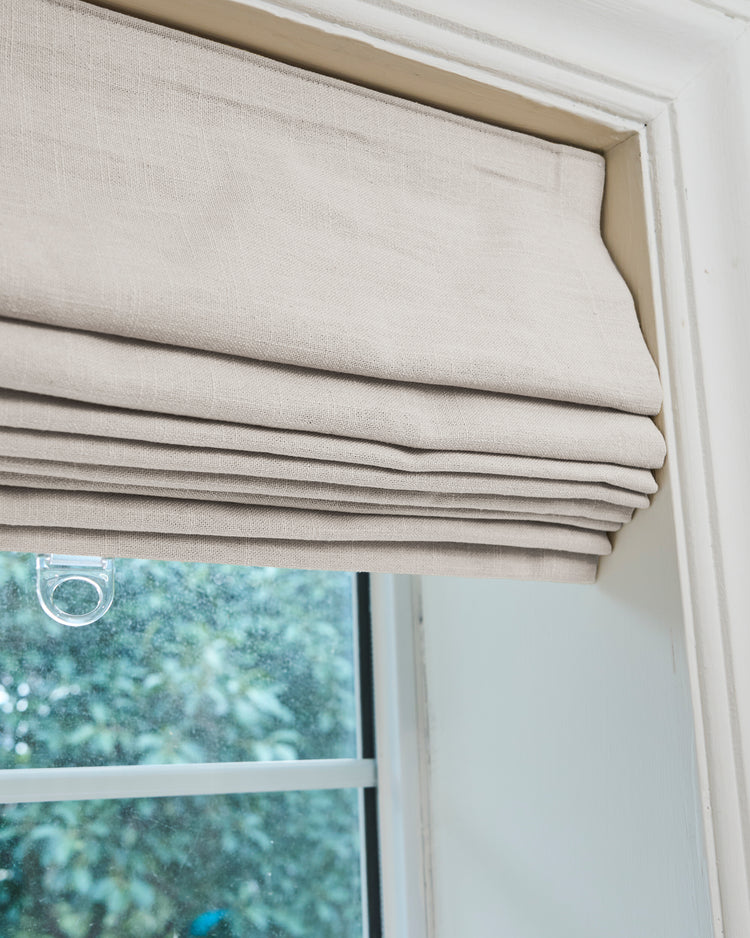 Textured beige Cassie Flat Fold Linen Blend Custom Roman Shade installed in a window frame, offering tailored light control.