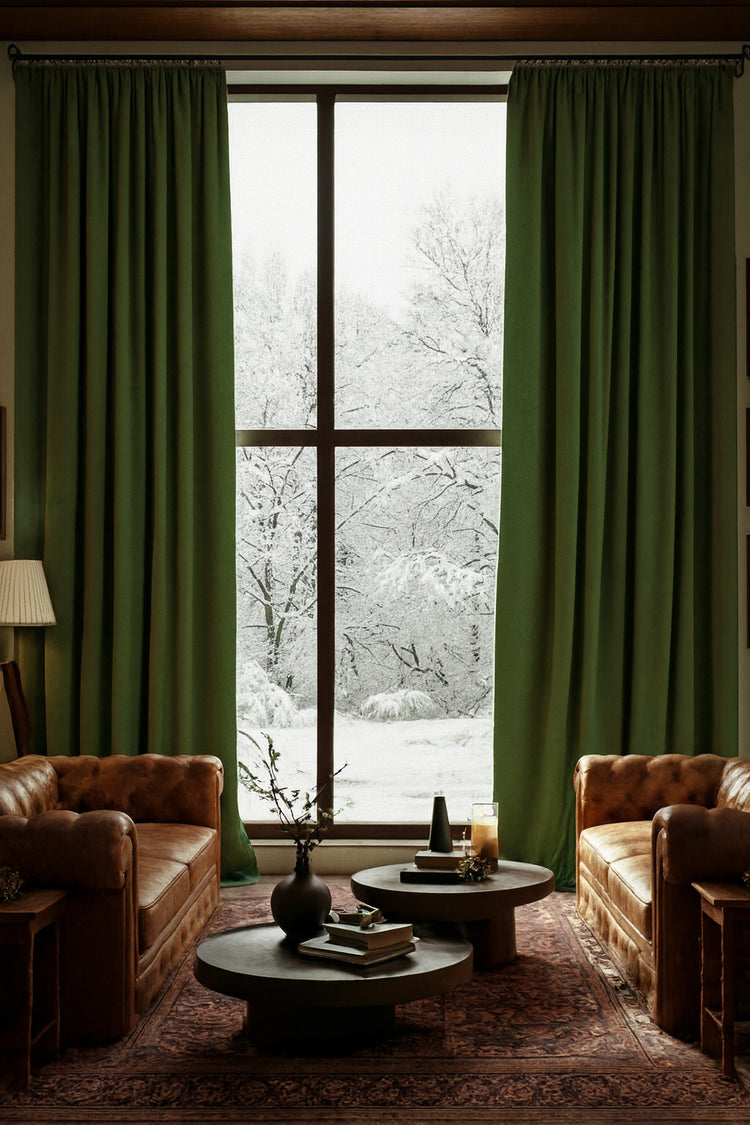 Lush green velvet custom curtains frame a large window with a snowy landscape. Tailored window treatments for elegant home decor.