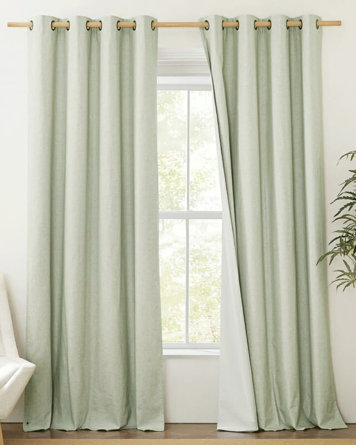 Custom Cronin linen-look blackout curtains in sage green with grommet headers, one panel open to show light-blocking privacy lining.