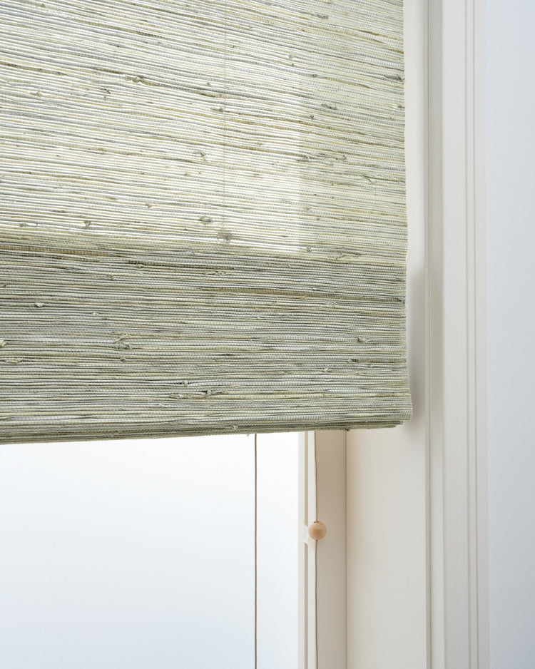 Close-up of a Mia Grey Jute Woven Shade, showcasing its natural textured weave and cord with wooden toggle for light control.