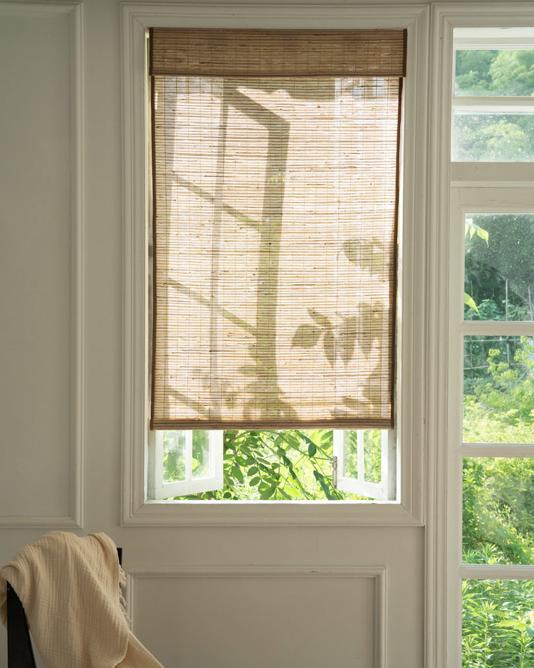 Ecru Mia Jute Woven Shade on a white window, beautifully filtering sunlight and casting leaf shadows, for elegant light control.