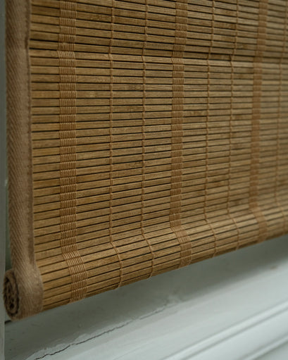 Close-up of a tan Hana bamboo woven shade, showcasing natural texture, horizontal slats, and rolled bottom for light control.
