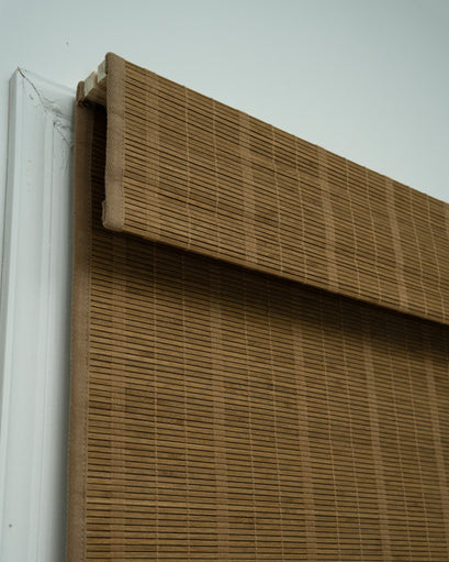 Close-up of a tan Hana bamboo woven shade, highlighting its natural woven texture and top header inside a window.