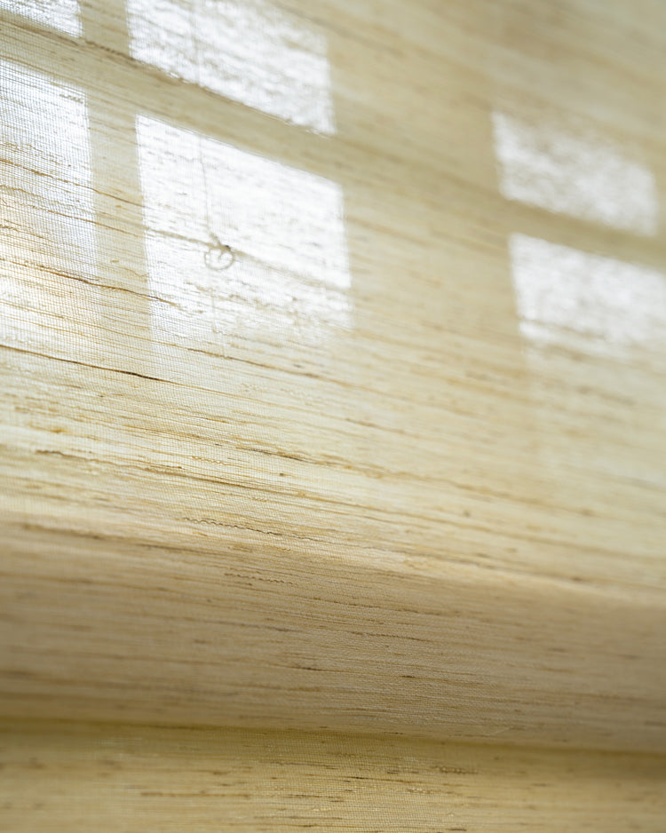 Natural Nico Jute woven window shade, close-up texture detail with filtered sunlight creating soft patterns through the fabric.