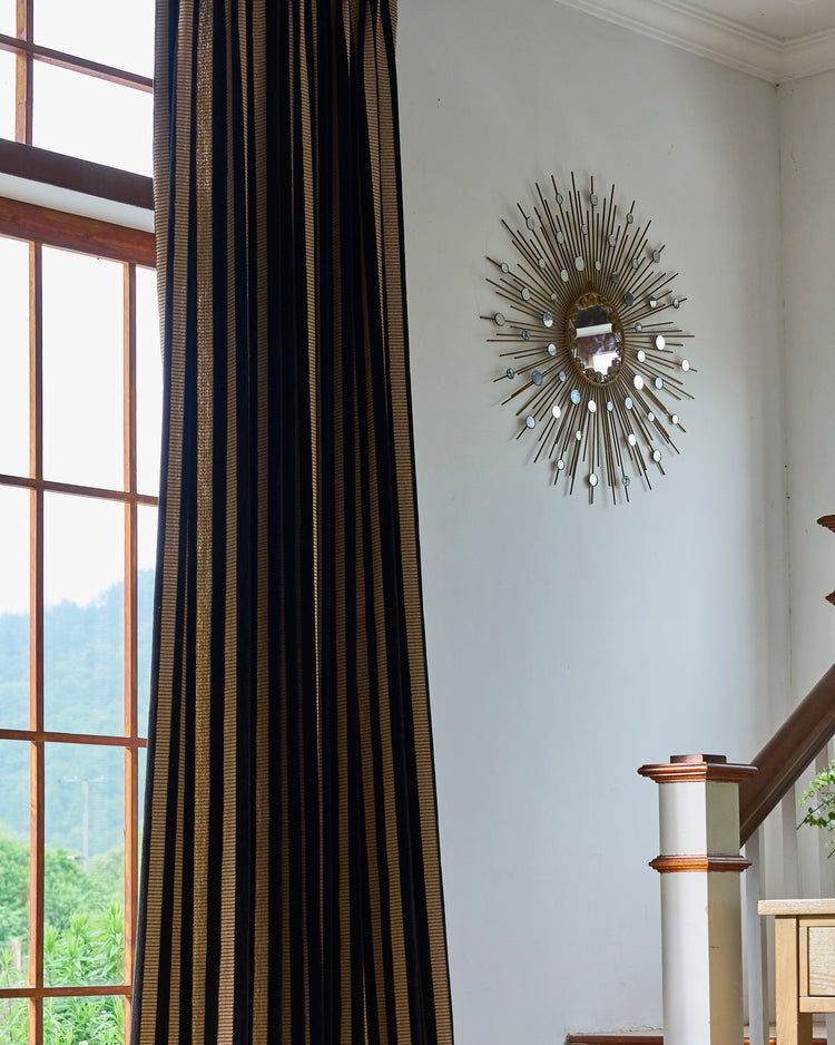 Liam Striped Linen Blend Custom Curtain, black & gold, next to a wooden window frame; decorative sunburst mirror on wall.