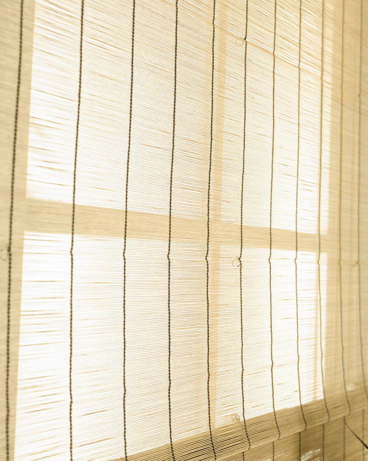 Close-up of a light Toni Bamboo Woven Shade detail, showing natural woven texture and vertical cords as sunlight filters through.